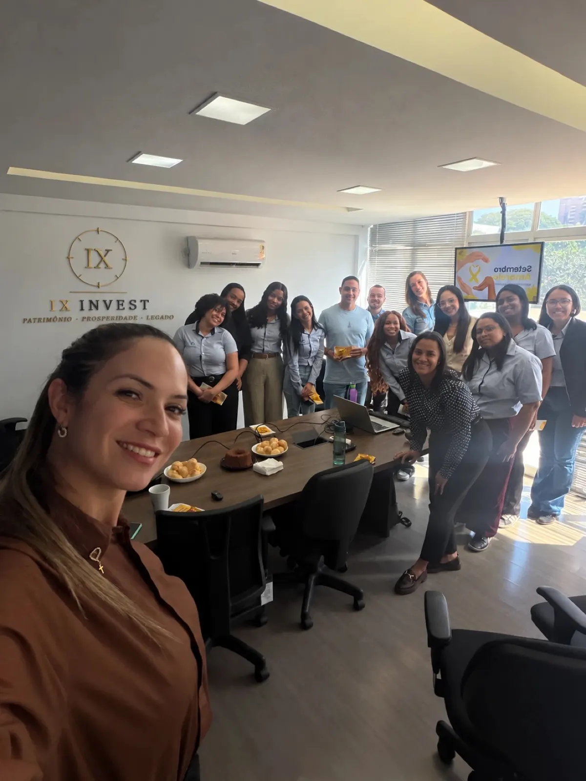 Ingrid Xavier com a equipe da IX Invest na sala de reuniões do escritório, com o logo da empresa na parede